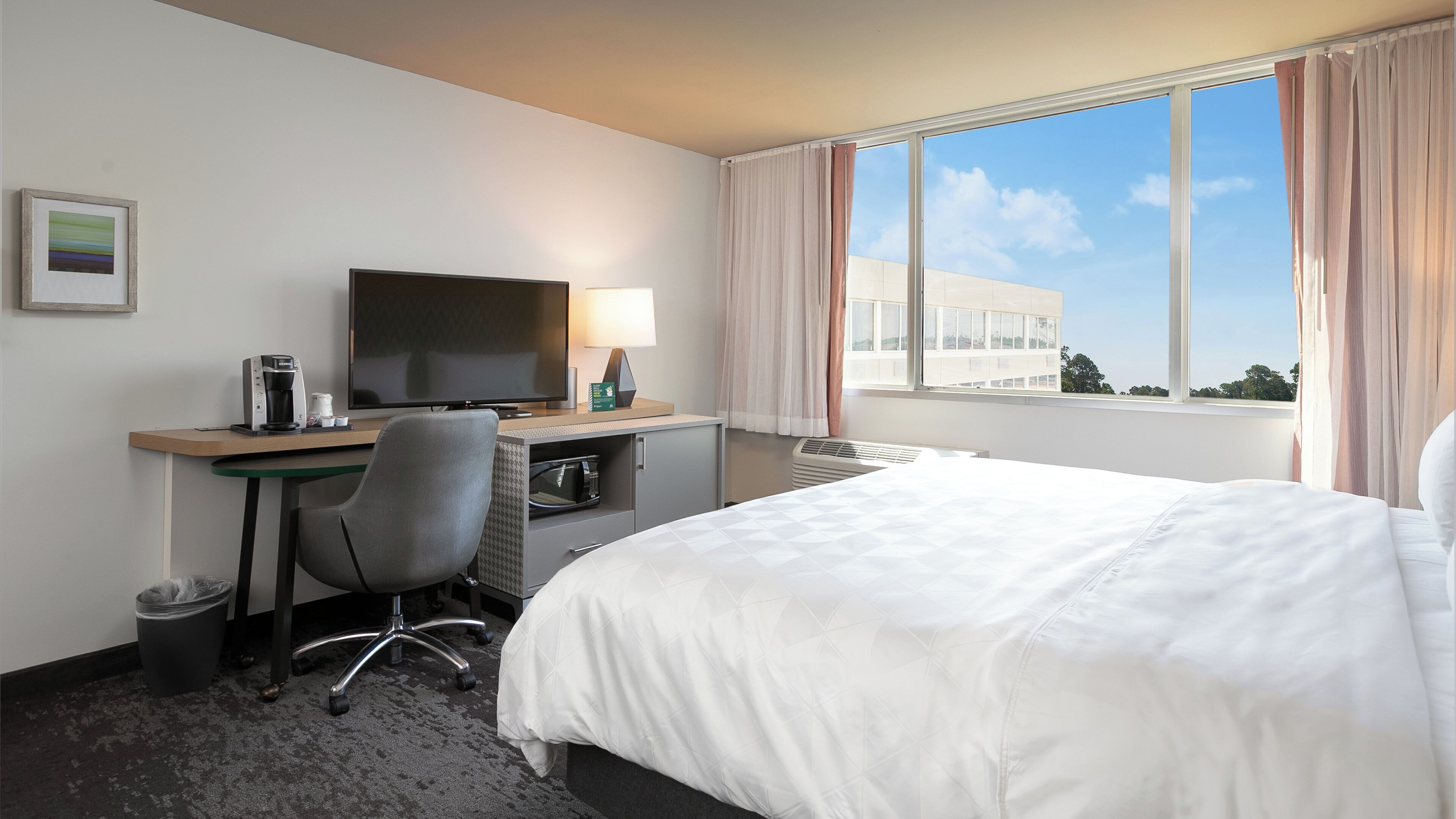 Een hotelkamer met een bed, bureau, stoel, televisie en een raam met gordijnen.