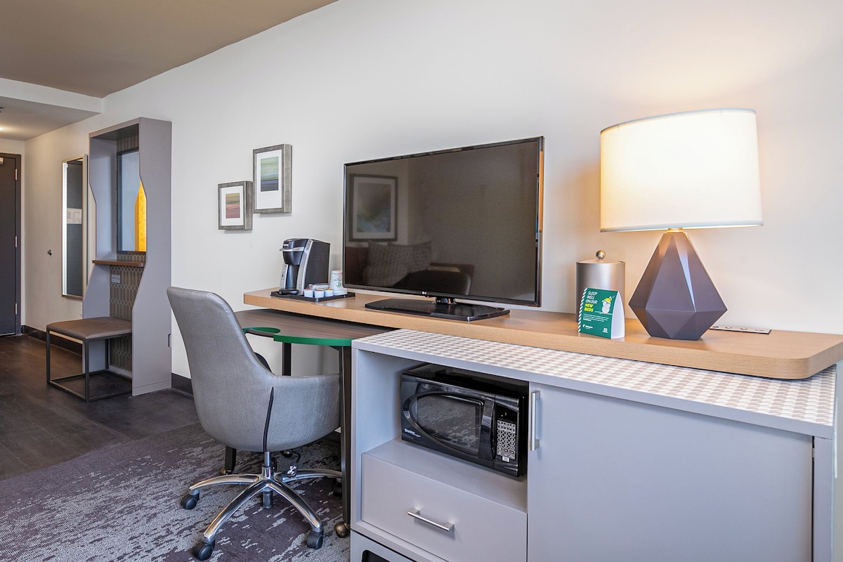 A hotel room with a desk, chair, television, lamp, and a microwave.
