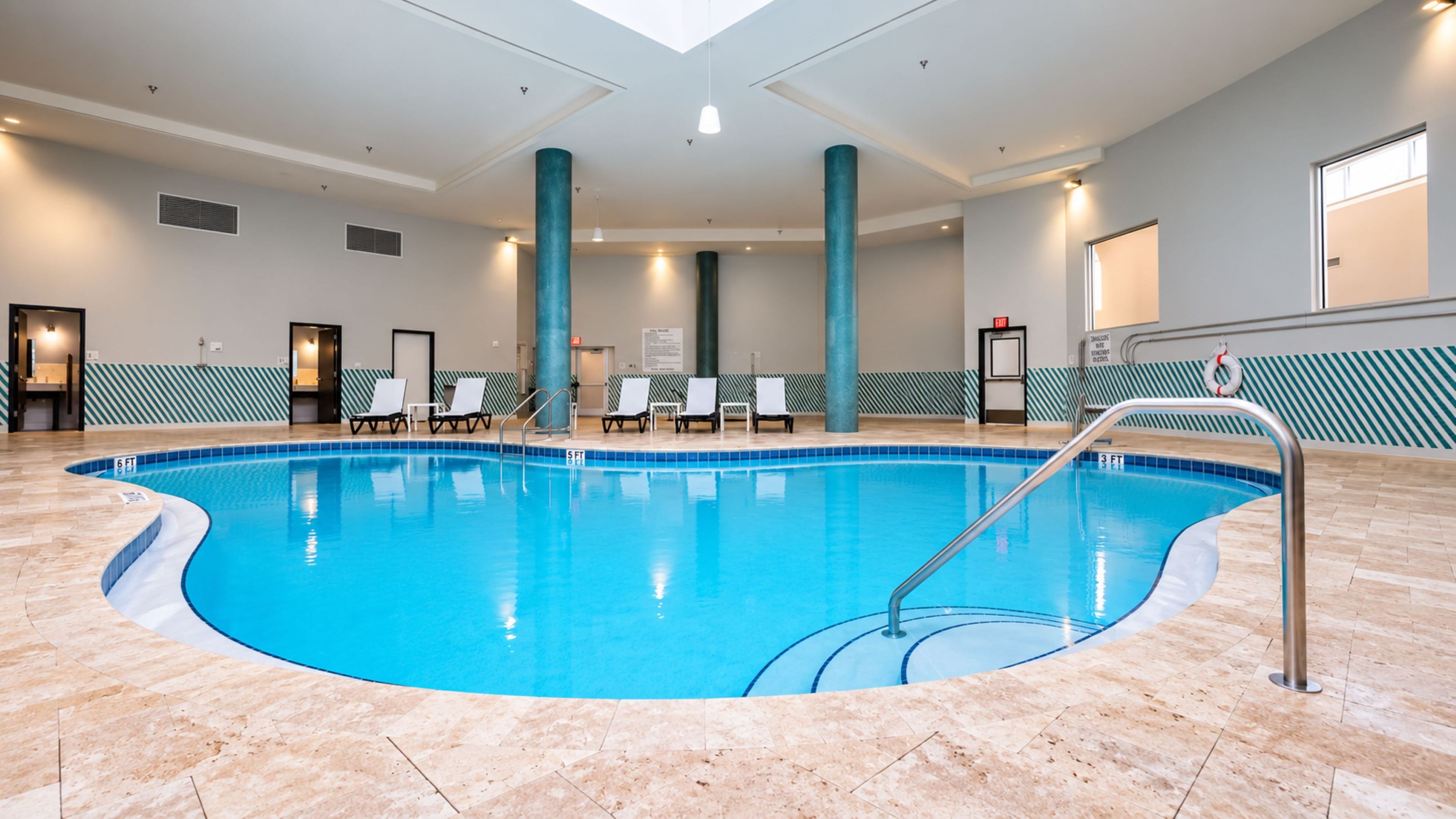 Una piscina interior con agua cristalina, rodeada de sillas de descanso y un suelo de baldosas.