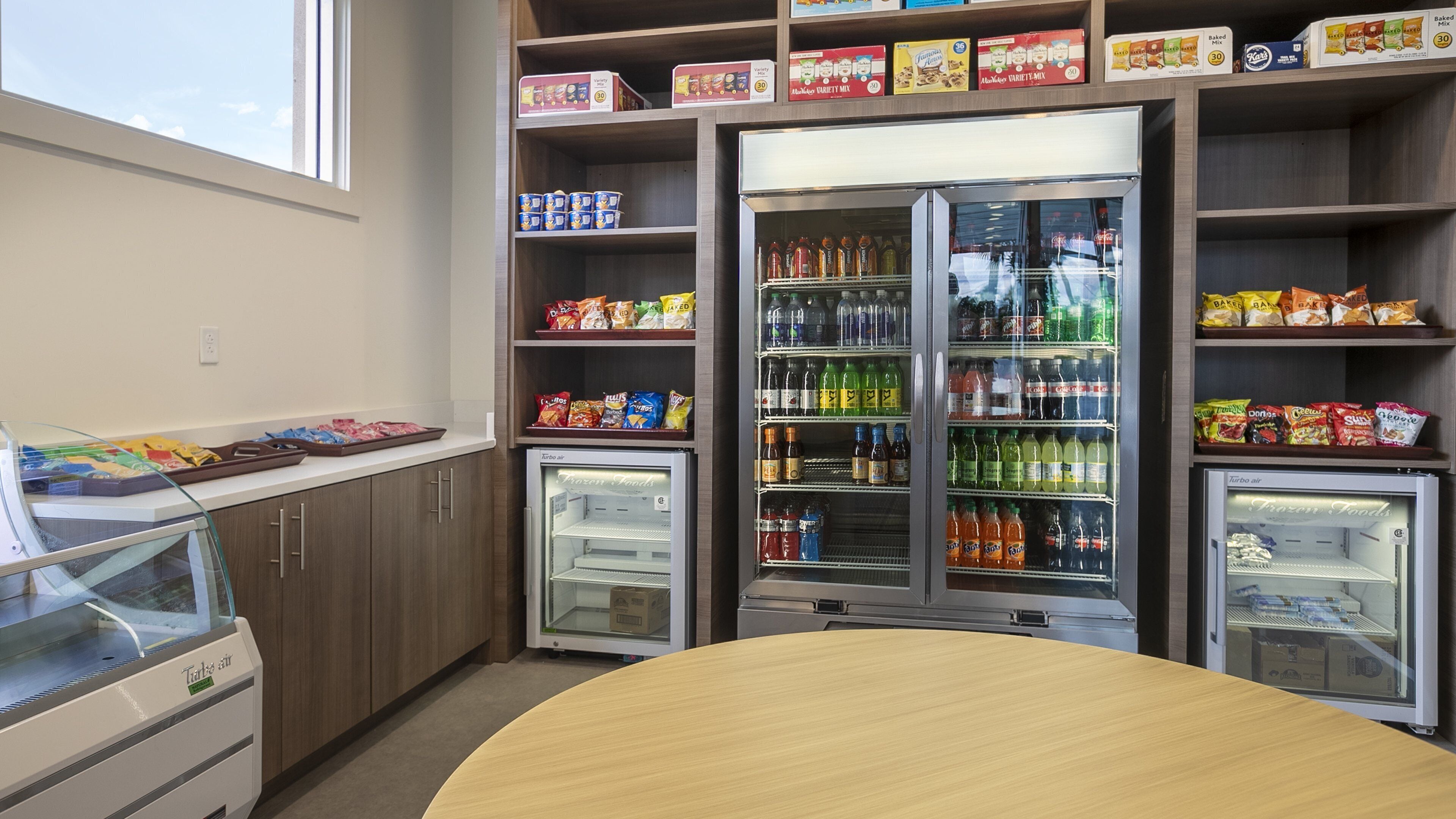 A self-service food area with refrigerated beverage dispensers, snack shelves, and a freezer.