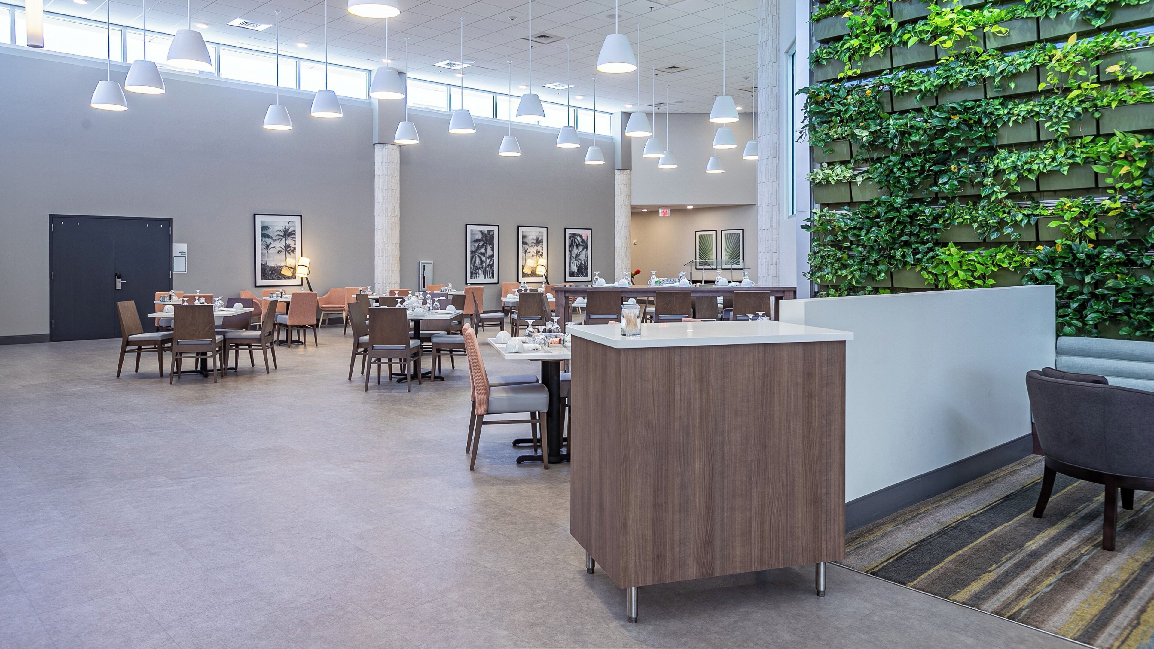 A spacious dining area with multiple tables and chairs, pendant lighting, and a green vertical garden wall.