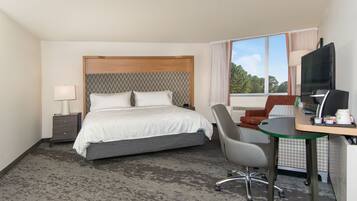 A hotel room with a bed, a desk with a computer, a chair, and a TV.