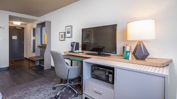 Et hotelværelse med skrivebord, stol, computer, lampe og mikroovn.