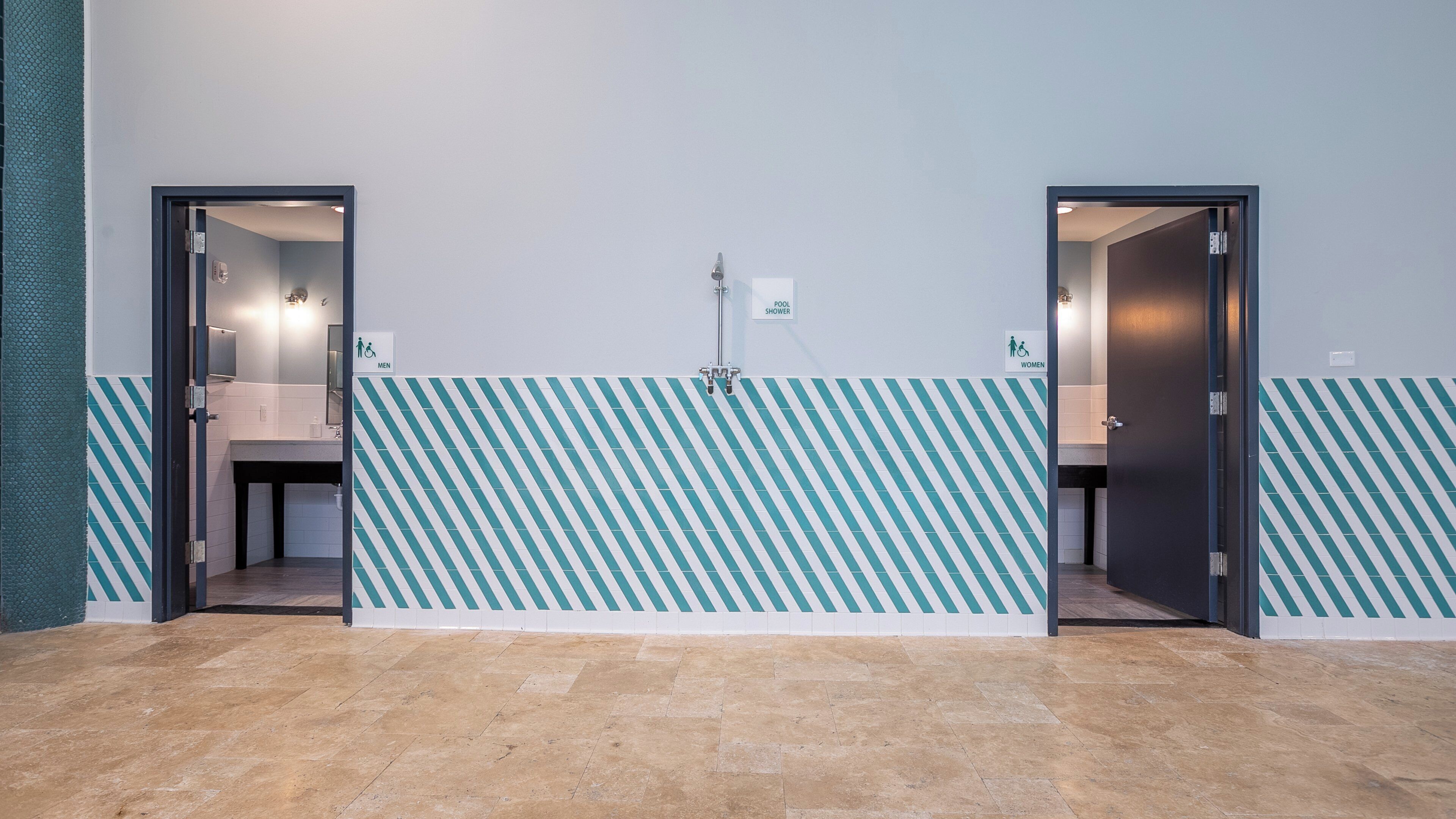 A restroom with two doors, one labeled 'MEN' and the other 'WOMEN,' and a 'POOL SHOWER' sign above the doors.