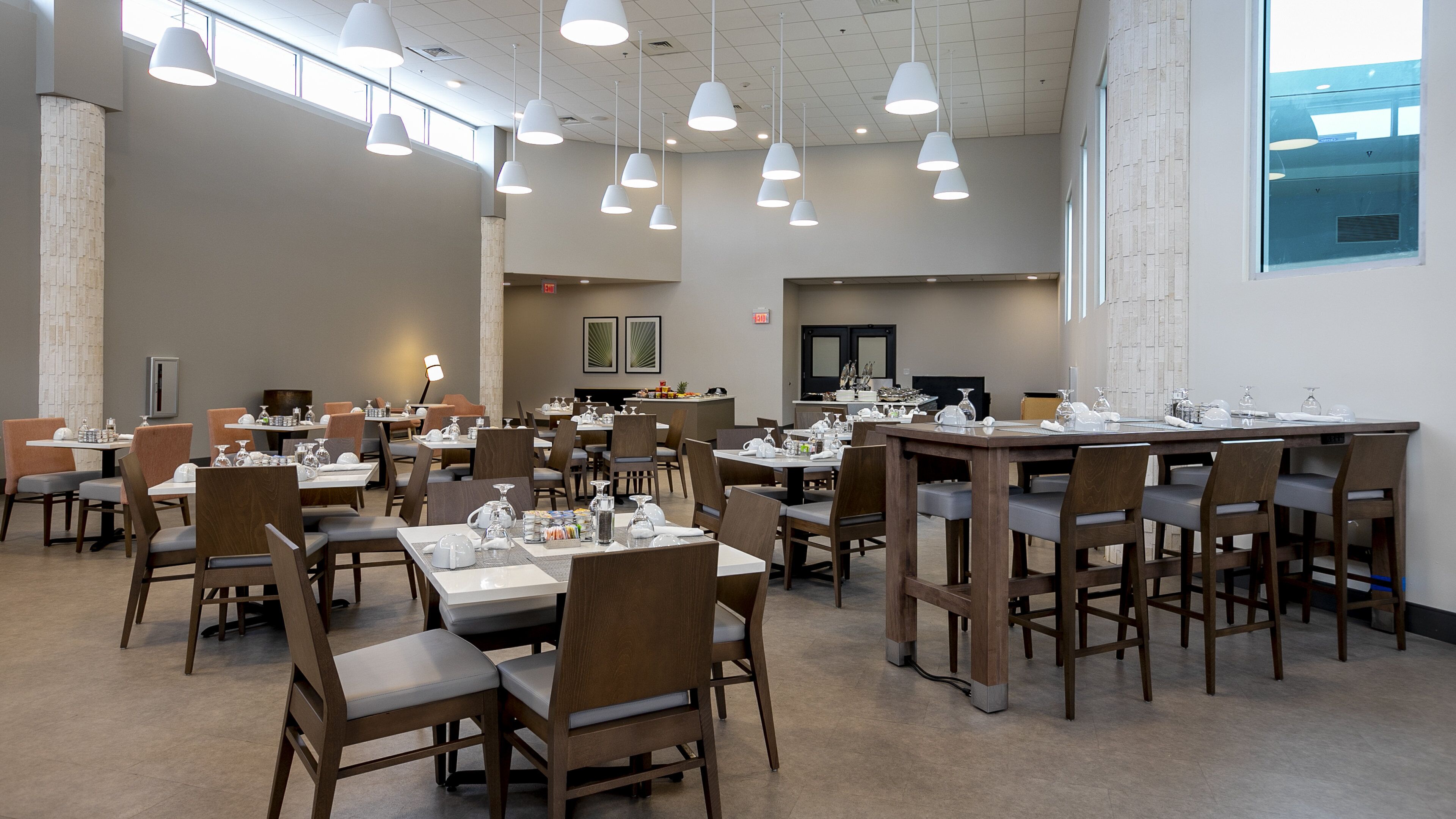 A spacious dining area with multiple tables and chairs, overhead lighting, and a large window providing natural light.