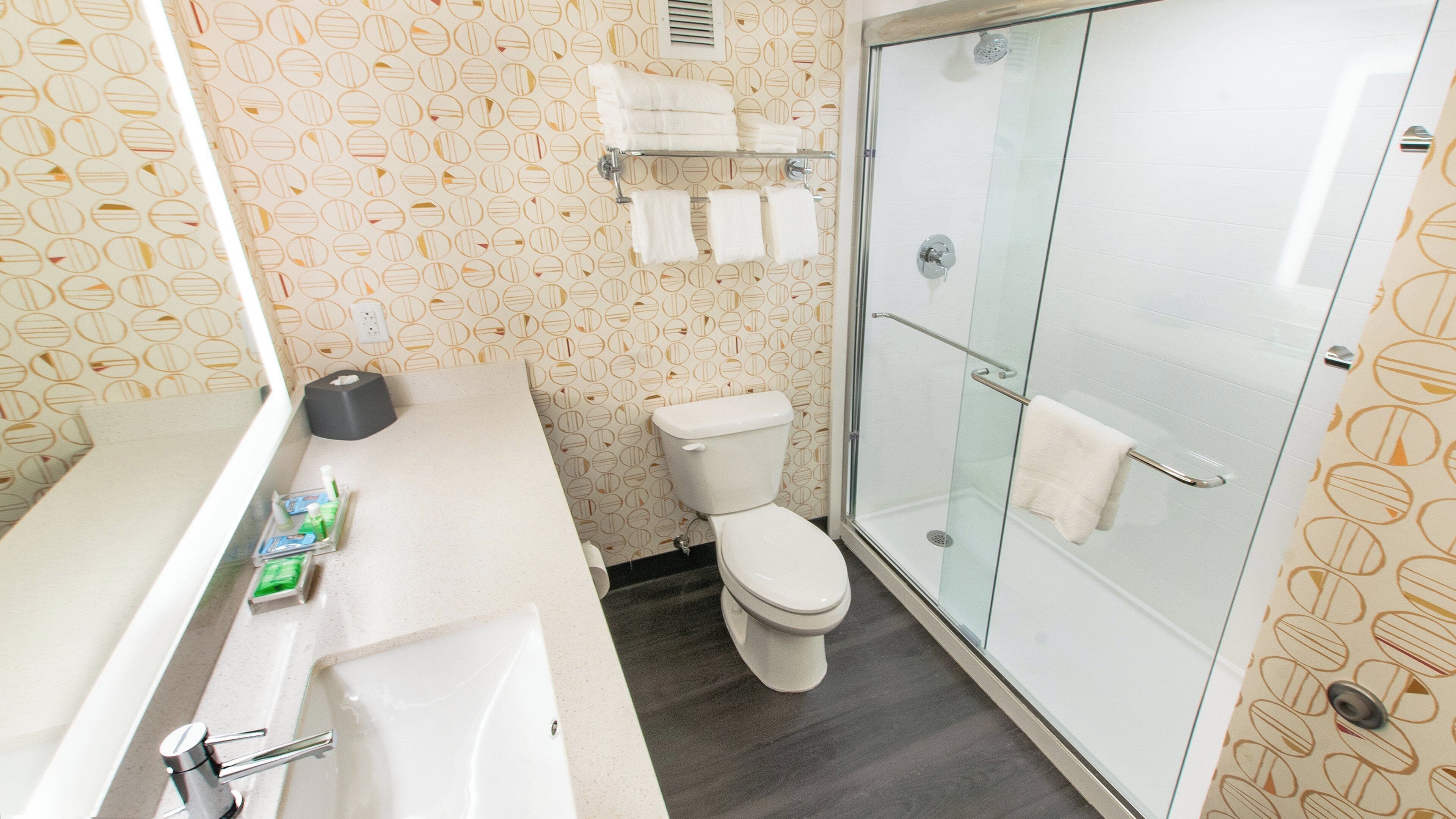 A bathroom with a toilet, a glass shower enclosure, a sink, and a towel rack.
