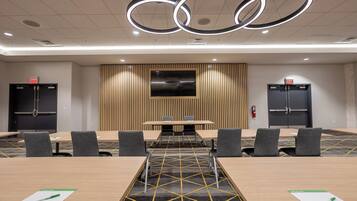 A conference room with a long table, six chairs, a large screen, and two black cabinets with red exit signs.