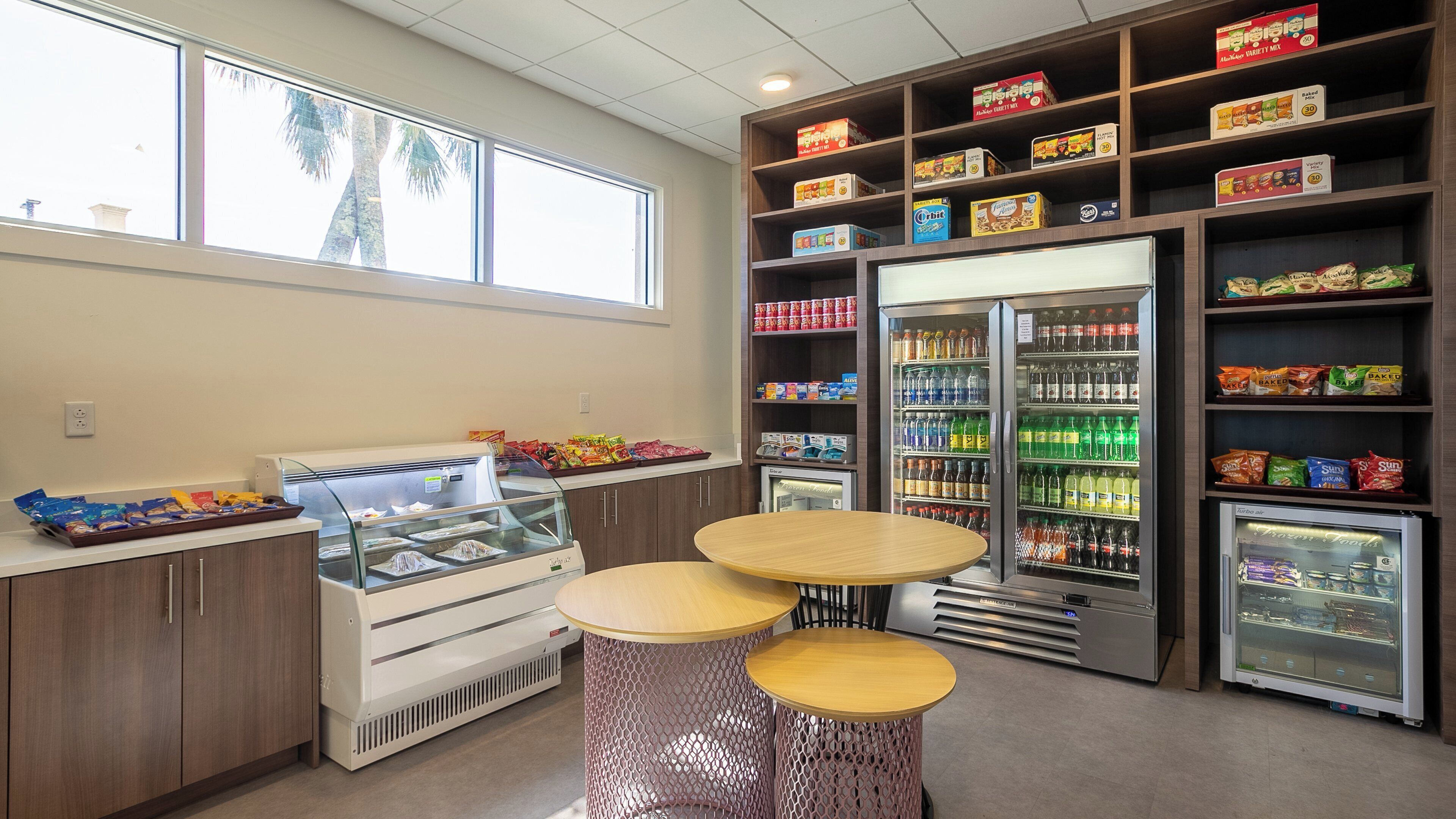 A snack bar with a variety of packaged snacks, a refrigerated display case, and a seating area with two round tables.
