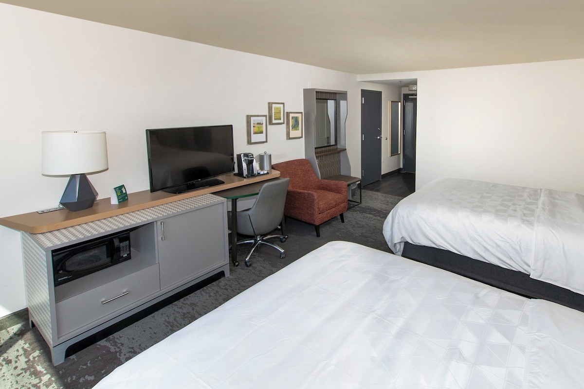 A hotel room with a bed, a desk with a computer, a chair, and a television.