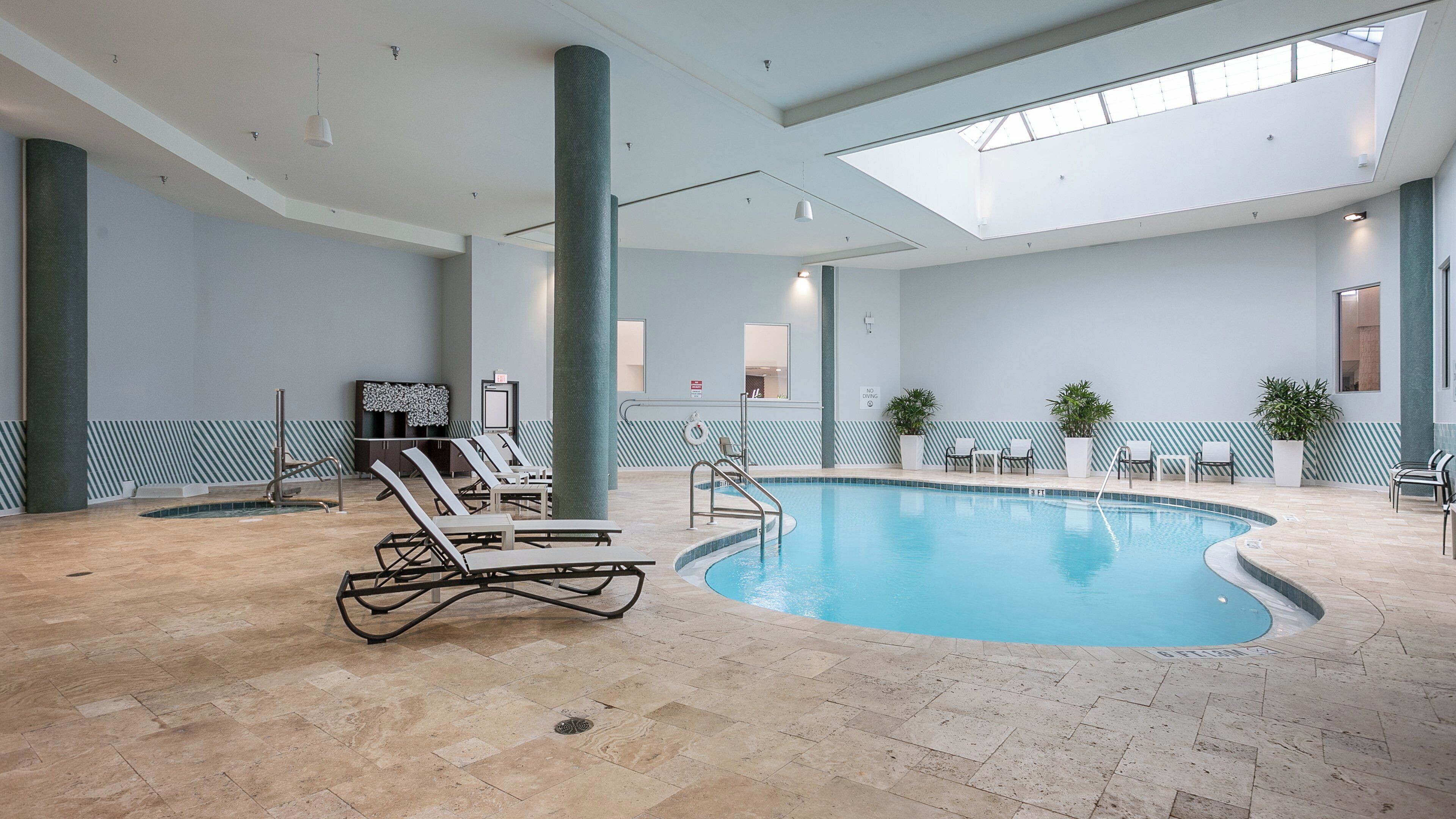 An indoor swimming pool with lounge chairs, a changing room, and a skylight.