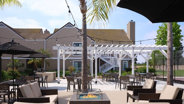 An outdoor patio area with wicker furniture, a fire pit, and a covered seating area with umbrellas. - Residence Inn by Marriott Costa Mesa Newport Beach (Costa Mesa)