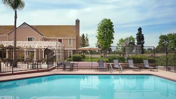 A swimming pool with lounge chairs and a fence, surrounded by a building and trees.