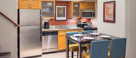 A compact kitchen with stainless steel appliances, wooden cabinets, and a dining area with blue chairs.