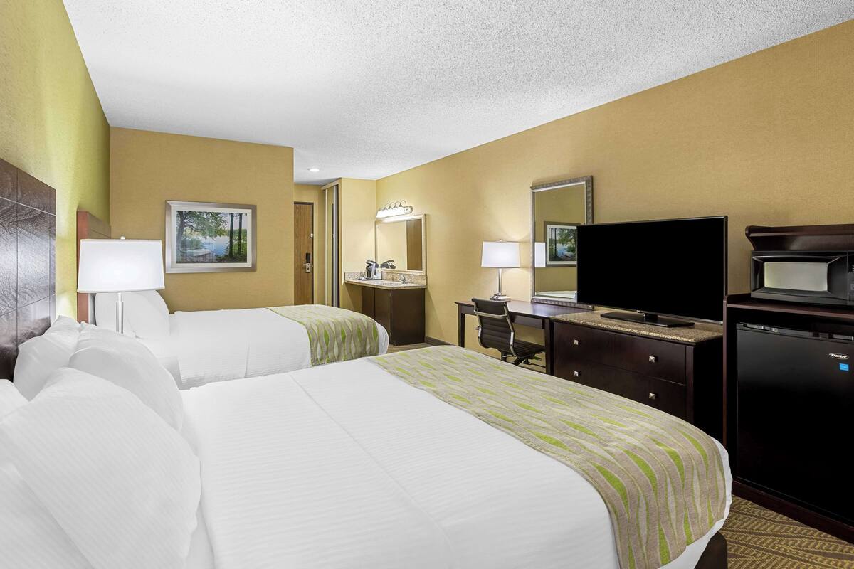 A hotel room with two beds, a desk, a television, and a minibar.