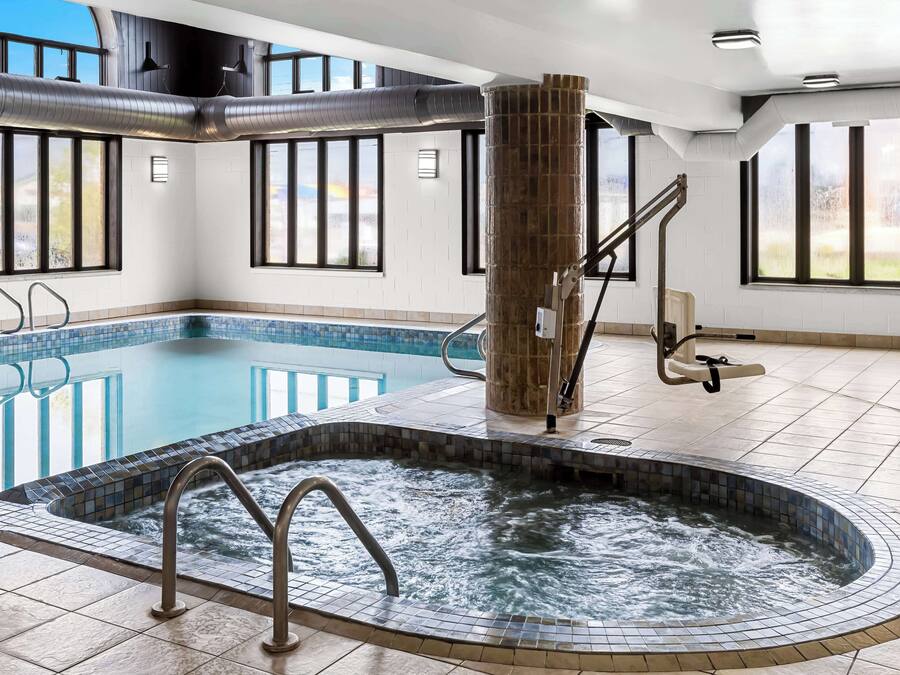A modern indoor pool with a hot tub, large windows, and a tiled floor.