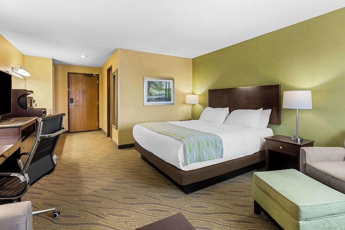 A hotel room with a large bed, a desk with a chair, a television, and a door leading to another room.