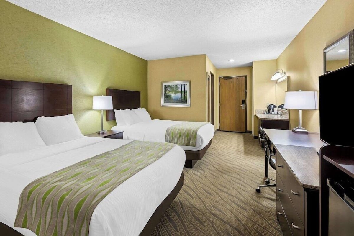 A hotel room with two beds, a desk, a chair, a television, and a bathroom.