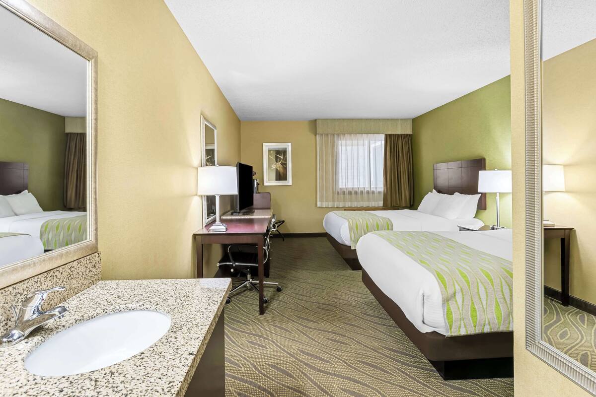 A hotel room with a large bed, a smaller bed, a desk with a computer, a sink, and a mirror.
