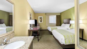 A hotel room with a large bed, a smaller bed, a desk with a computer, a sink, and a mirror.
