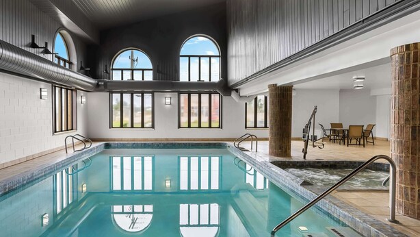Piscina interna com água cristalina, cercada por janelas e uma área de estar com cadeiras e mesa.