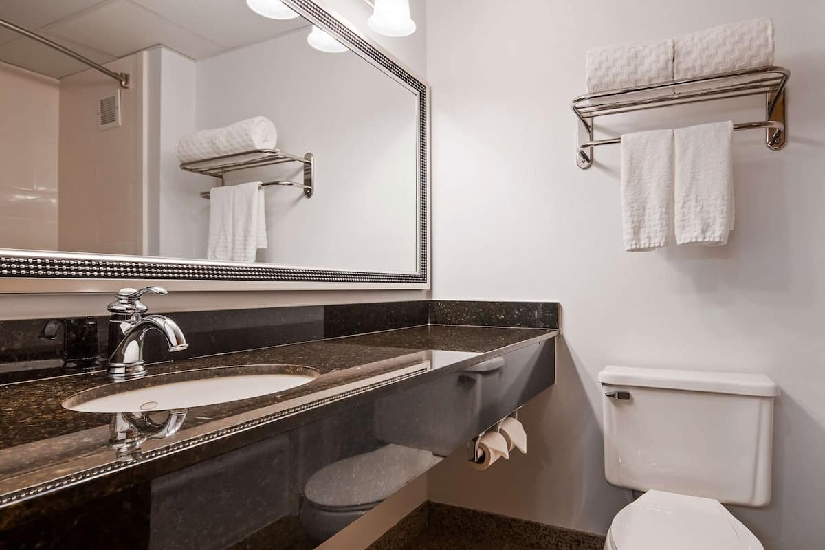 A bathroom with a sink, mirror, towel rack, toilet, and shower area.