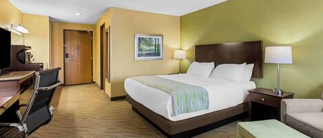 Quarto de hotel com uma cama grande, uma escrivaninha com cadeira, uma mesa pequena e um abajur.
