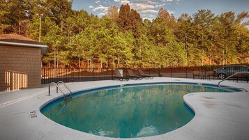 Una piscina con borde curvo, rodeada de una valla y árboles.