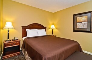 A hotel room with a large bed, two bedside tables with lamps, a nightstand, and a framed picture on the wall.