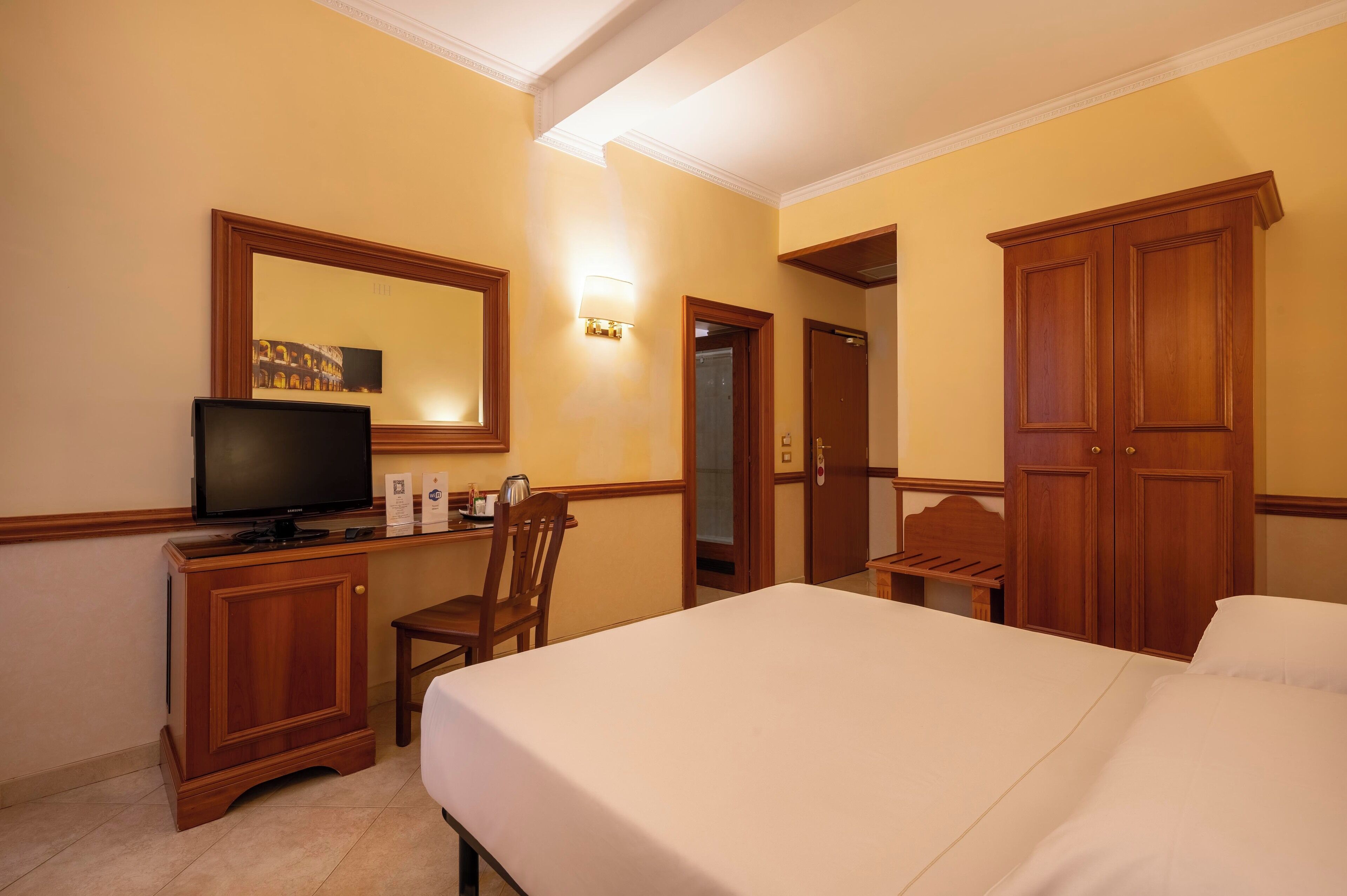 Une chambre d’hôtel avec un lit, une télévision, une armoire en bois, une chaise et un bureau.