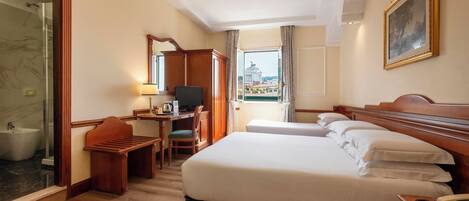 A hotel room with a bed, a desk with a chair, a television, a bathroom with a bidet, and a view of a building through a window.