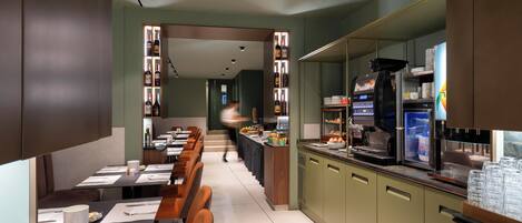 A modern restaurant with a long counter, dining tables, and a kitchen area with a coffee machine and refrigerator.