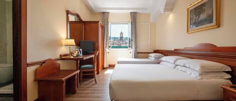 A hotel room with a large bed, a desk with a computer, a chair, and a view of a cityscape through a window.