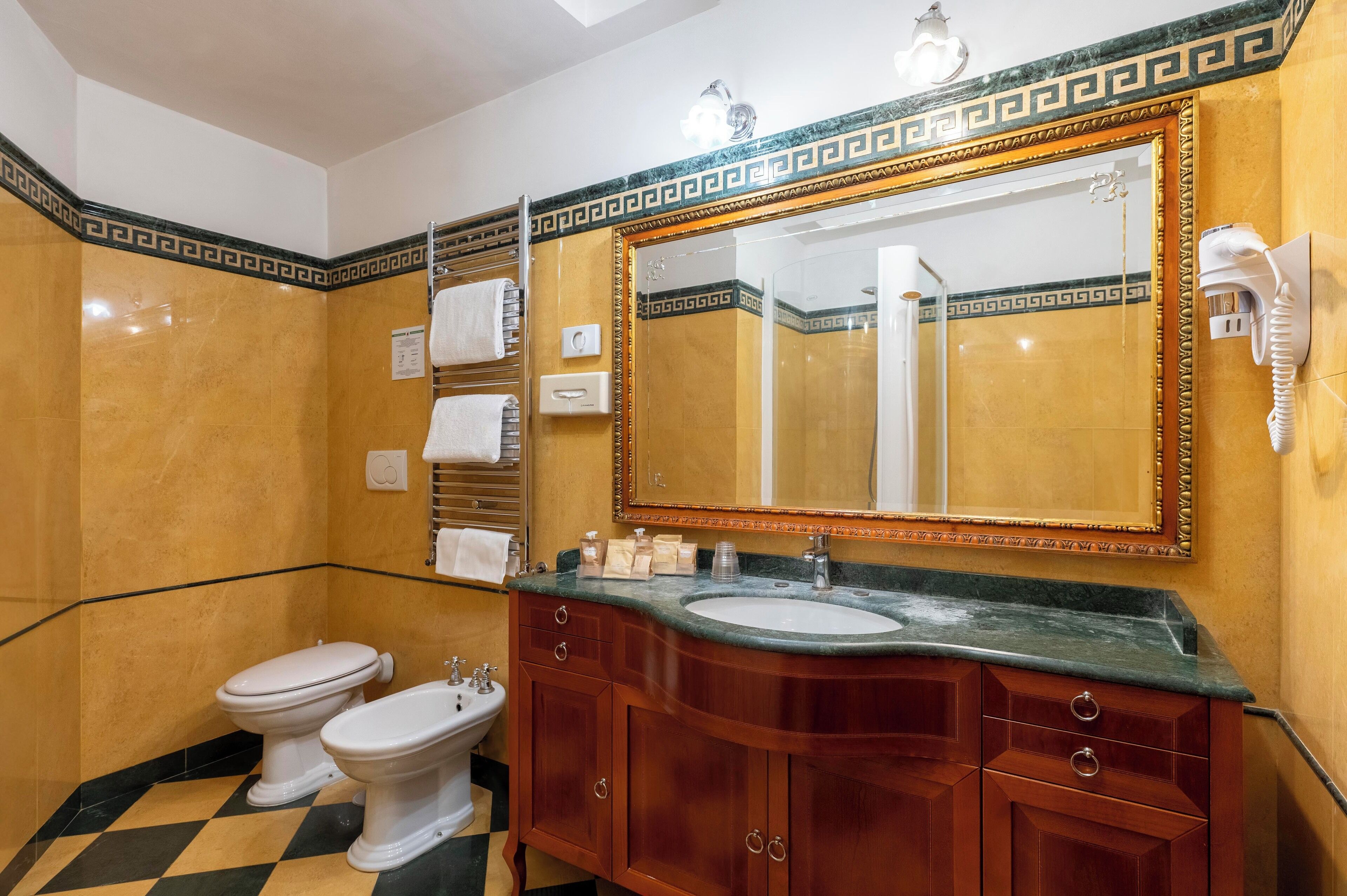 A bathroom with a marble vanity, two toilets, a sink, a large mirror, and a hairdryer on the wall.
