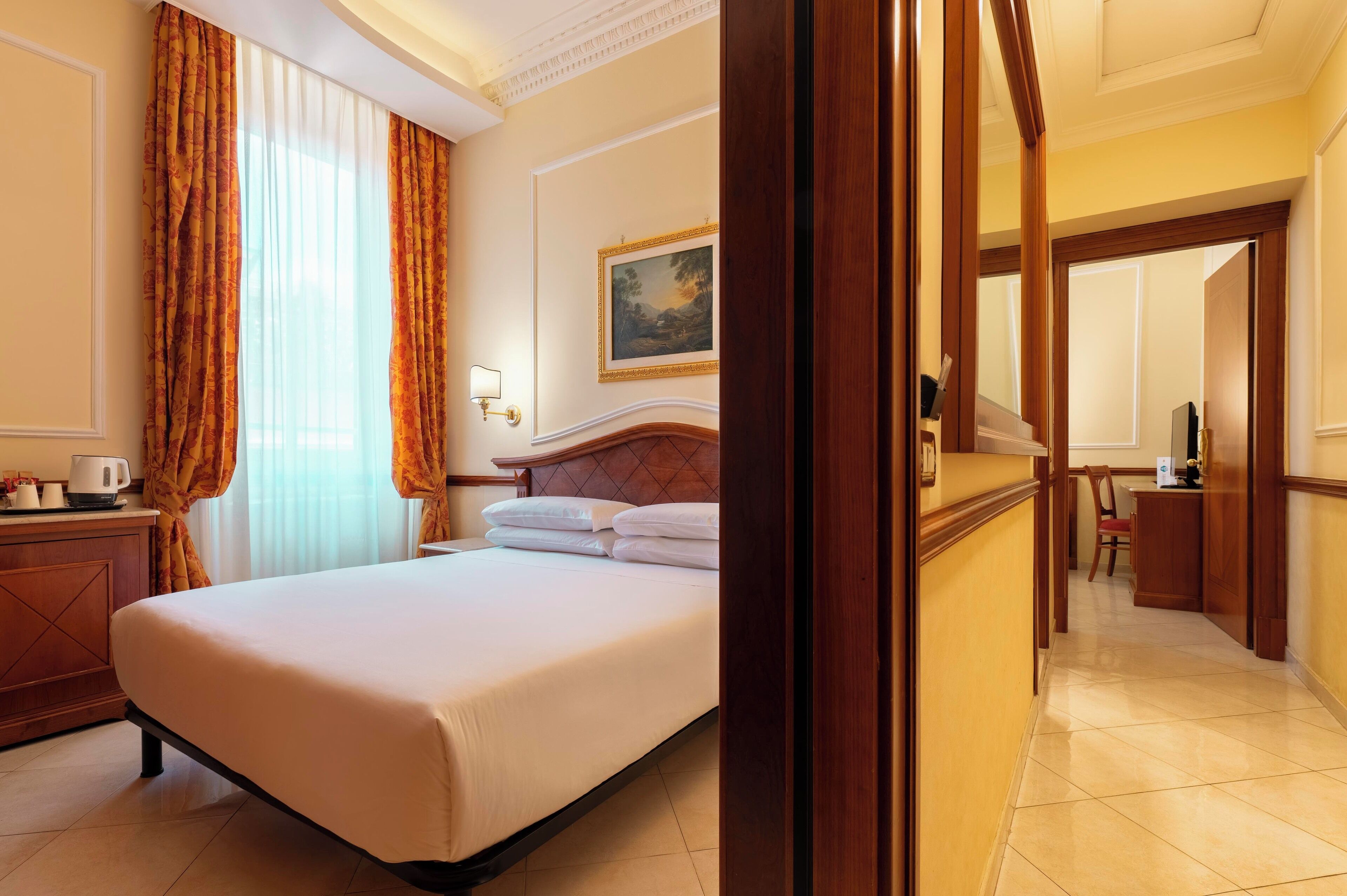 A hotel room with a large bed, a desk, and a painting on the wall.