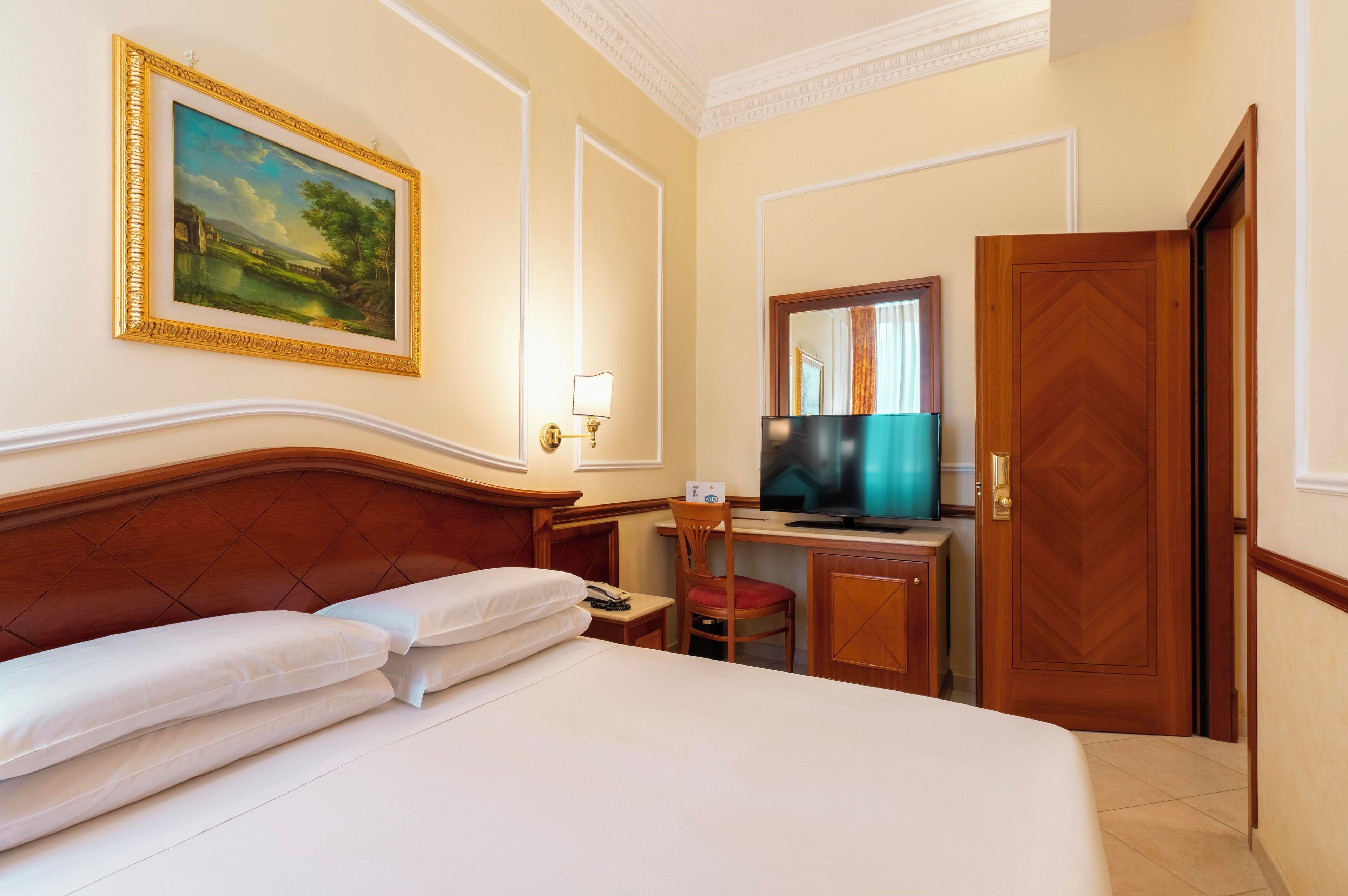 A hotel room with a large bed, a desk with a television, a chair, and a wooden door.