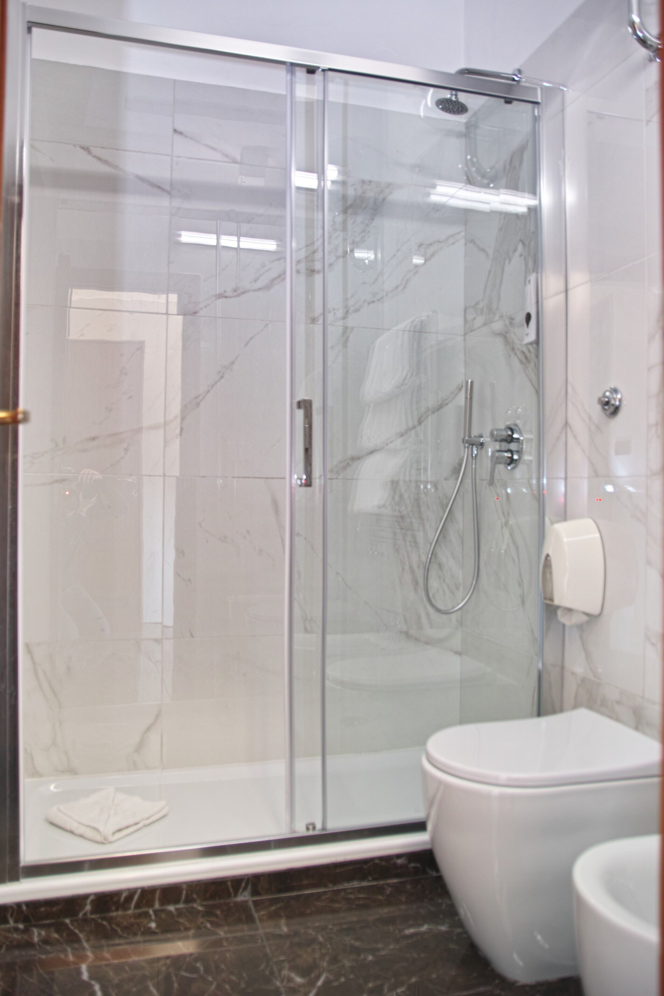 A modern bathroom with a glass-enclosed shower, a white toilet, and a marble-tiled floor.