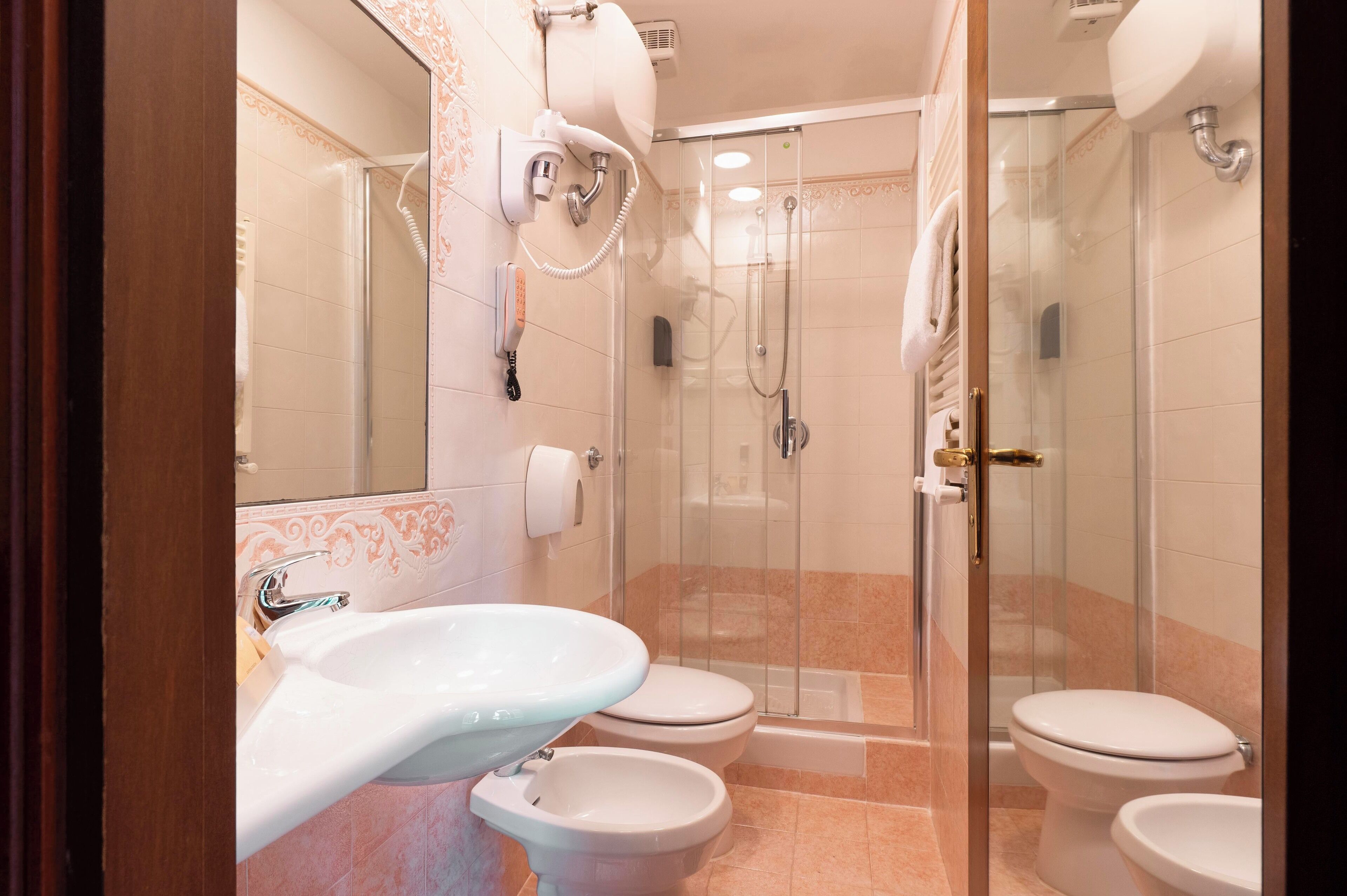 Une salle de bain avec une douche à parois de verre, trois toilettes et un lavabo.