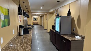 Un pasillo de hotel con encimeras de granito, armarios de madera oscura e iluminación colgante negra.