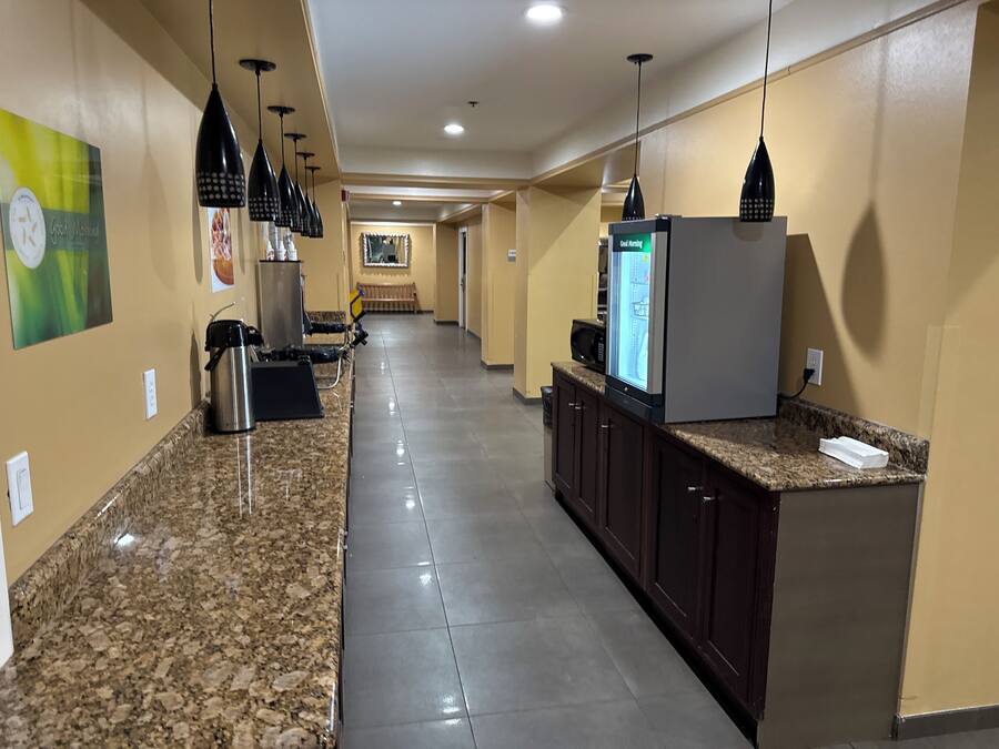 A hotel corridor with granite countertops, dark wooden cabinets, and black pendant lighting.