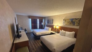 Habitación de hotel con dos camas, un escritorio, una silla y un televisor.