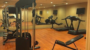 Un gimnasio con equipo de ejercicio, suelo de madera y un muro con espejos.