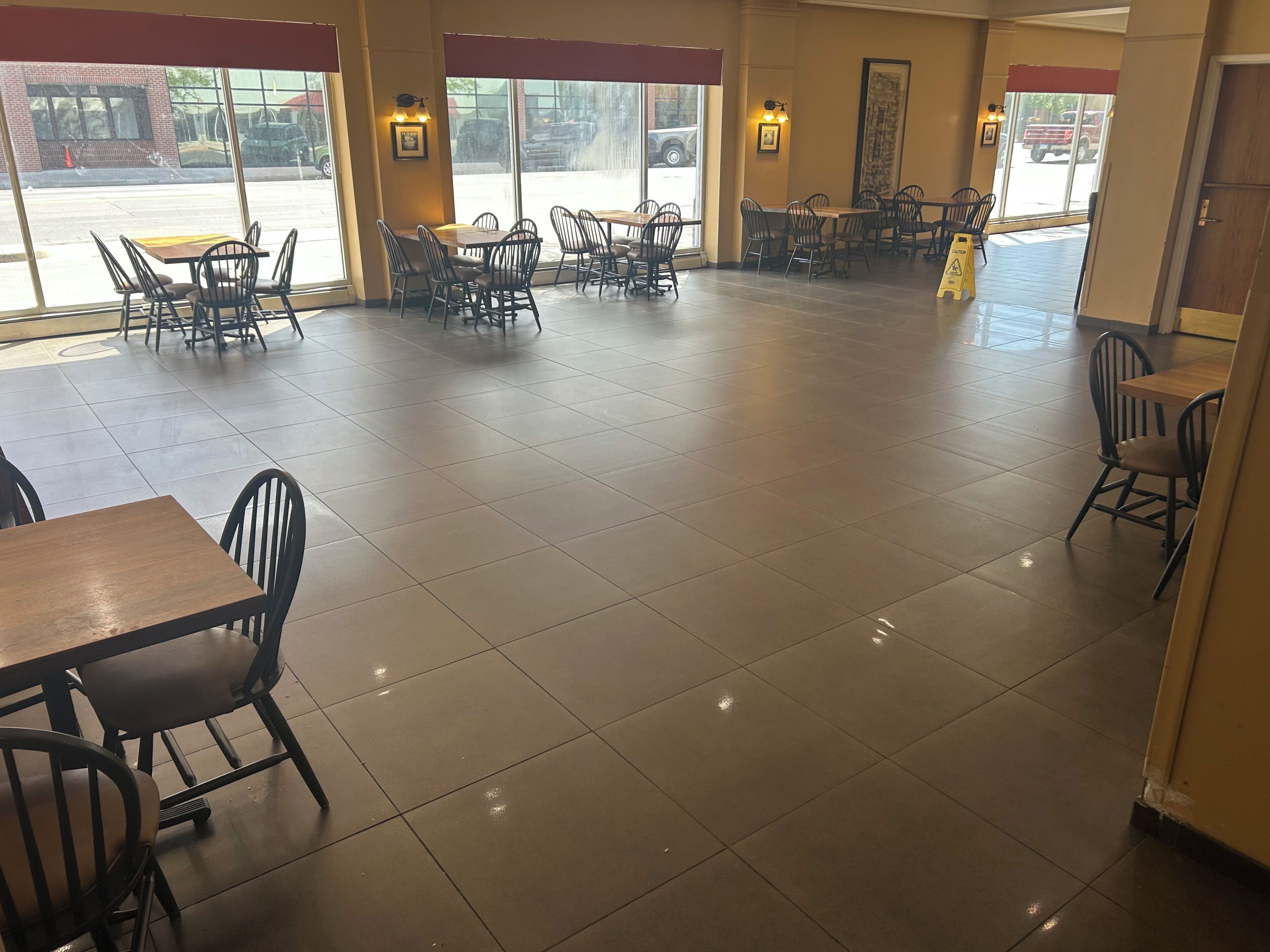 A spacious indoor area with multiple tables and chairs, large windows, and a tiled floor.
