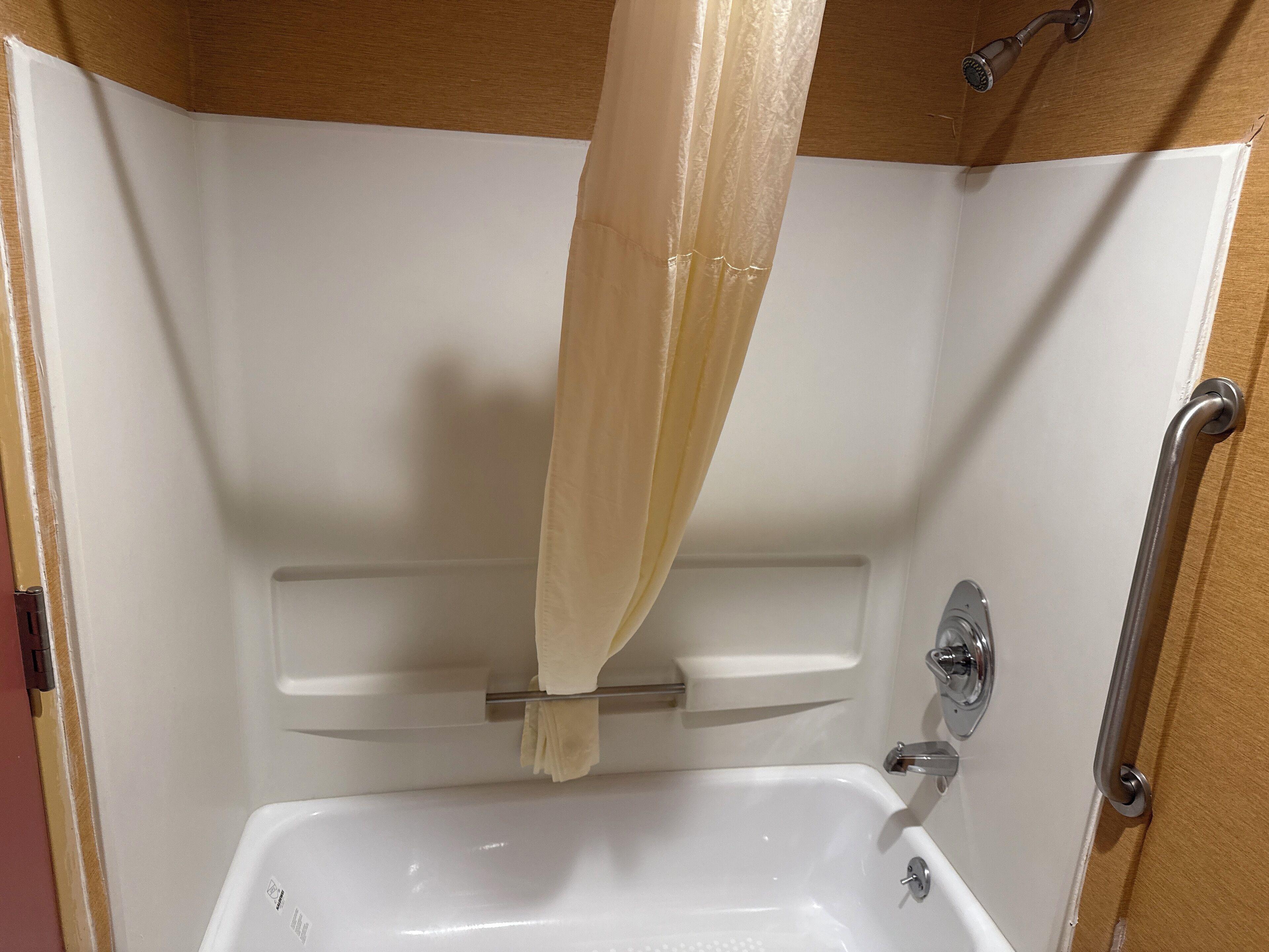 Baño con una bañera blanca, cortina de ducha y barra de apoyo.