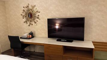 Camera d'albergo con una scrivania in legno, una TV a schermo piatto, un elemento decorativo a parete, una sedia e un letto.