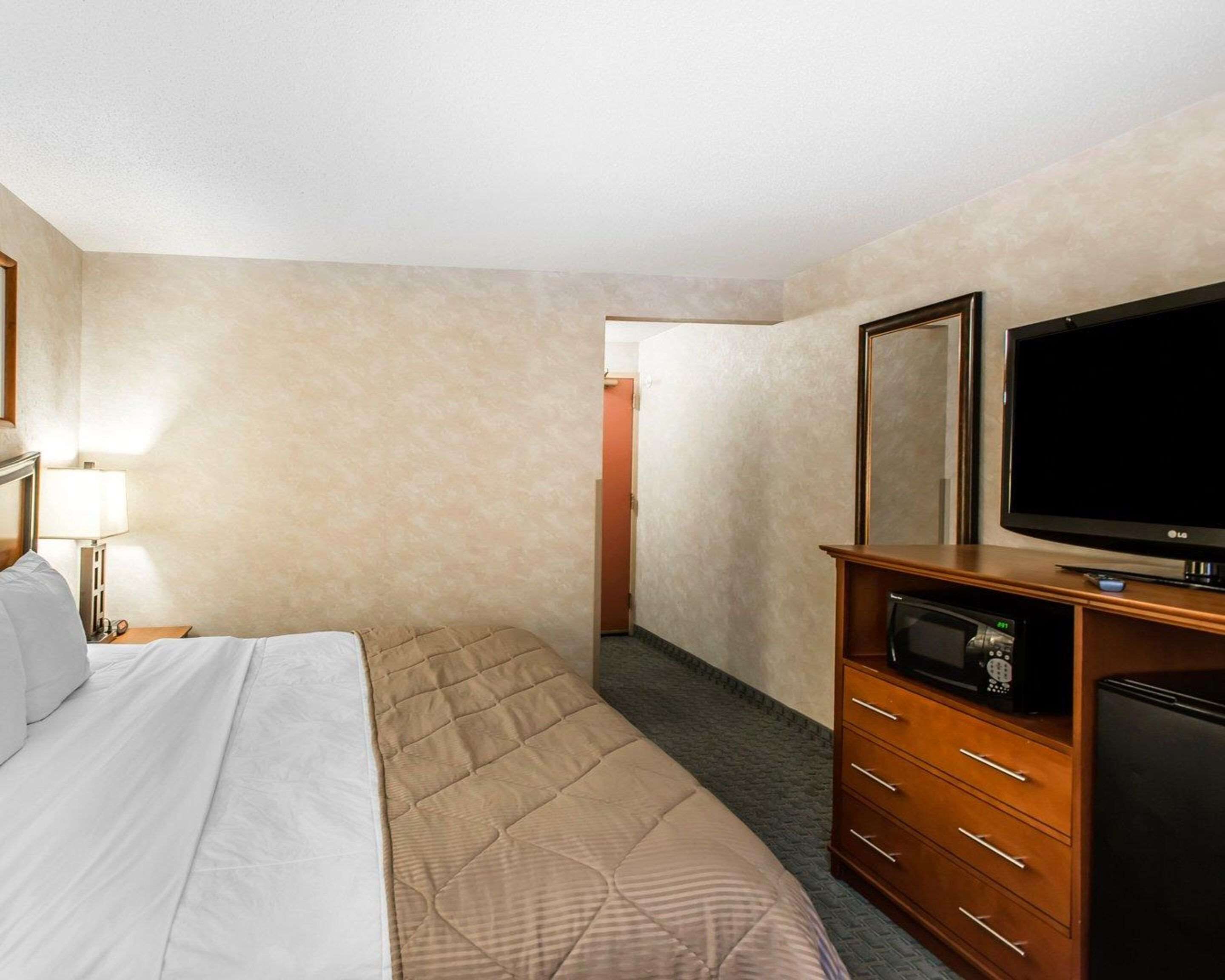 A hotel room with a bed, a television, a dresser, and a door leading to another room.