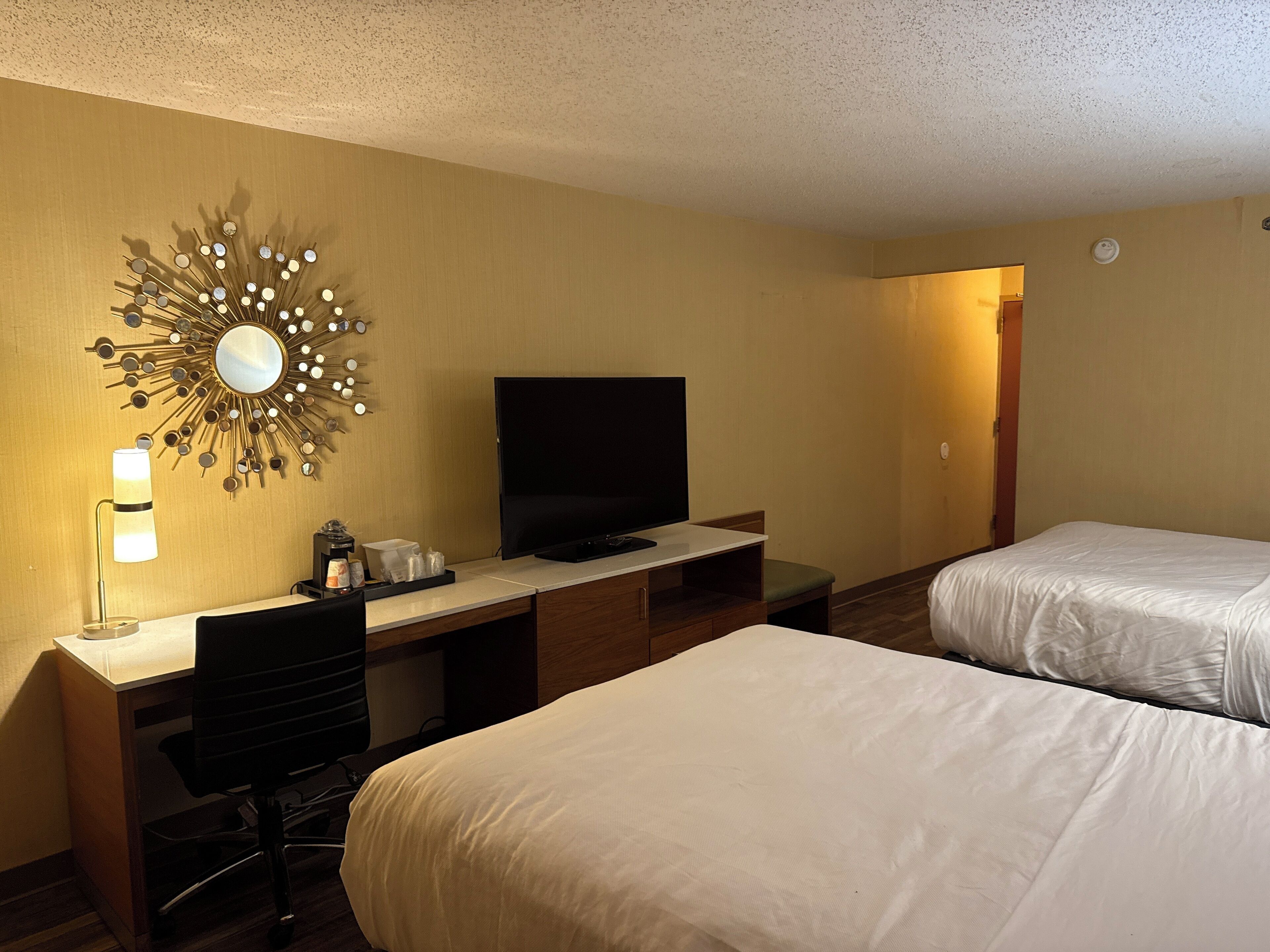 A hotel room with a desk, TV, two beds, and a decorative wall piece.