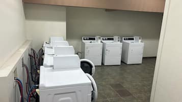 A laundry area with multiple washing machines and dryers, a tiled floor, and a white wall.