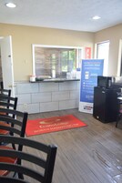 Interior de restaurante con mostrador, sillas, refrigerador y un cartel promocional.