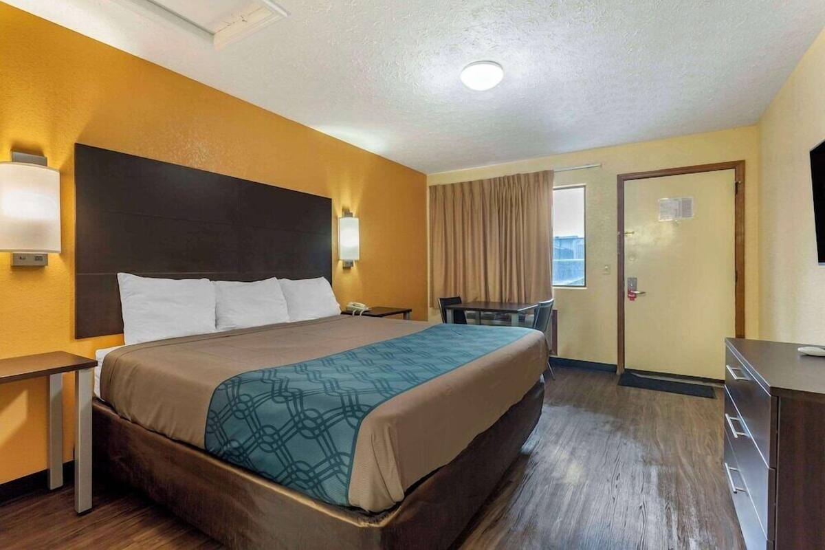 Ein Hotelzimmer mit einem Bett, einem Nachttisch, einer Lampe und einem Schreibtisch mit Stuhl.