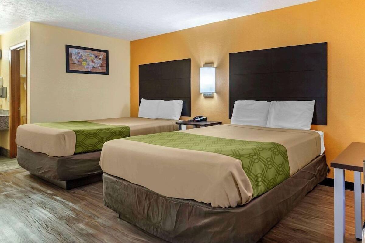 Ein Hotelzimmer mit zwei Betten, einem Nachttisch, einer Wandleuchte und einem gerahmten Bild an der Wand.